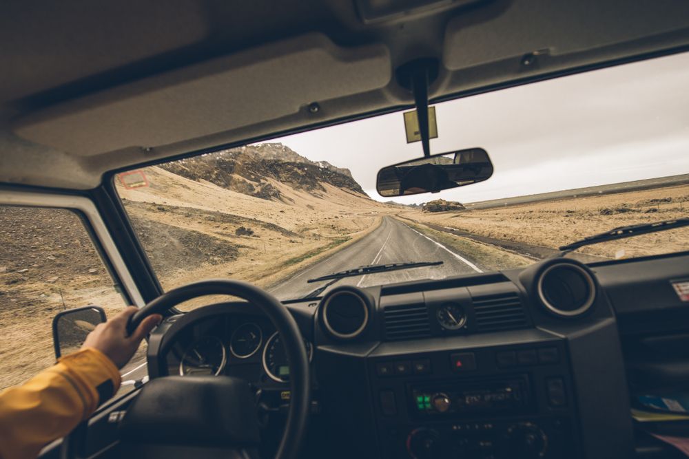  View from inside a rental car driving along a remote Icelandic road with rugged mountains in the distance.