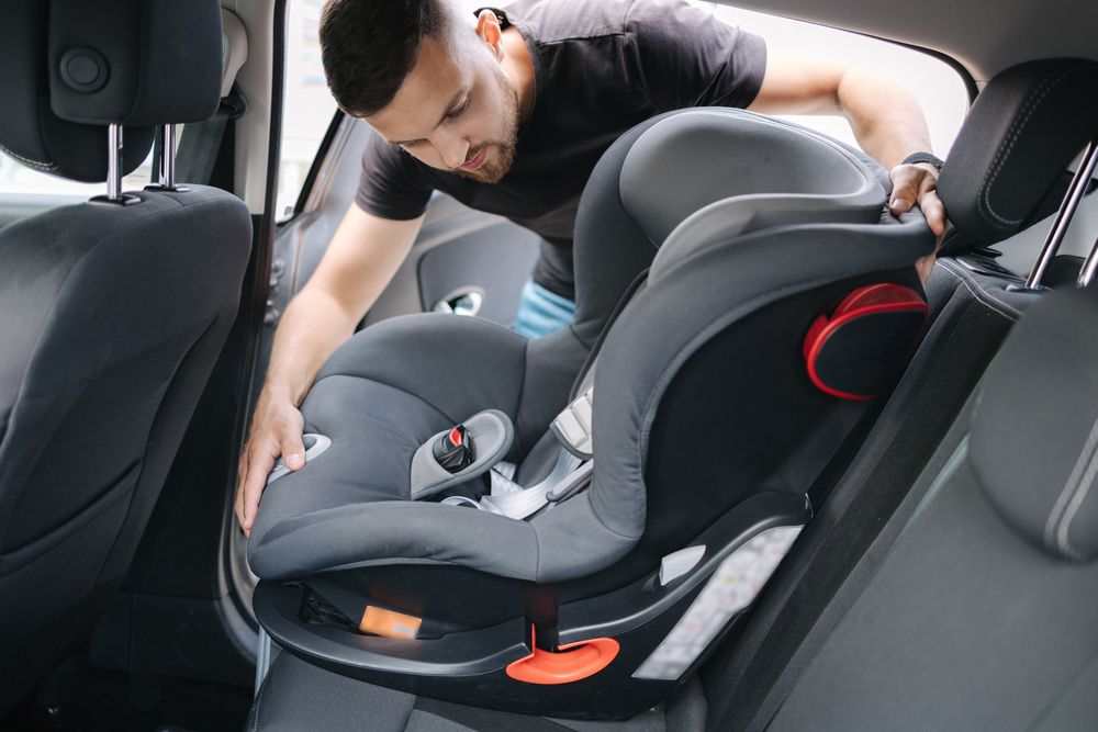 Man installing a child car seat in the back of a vehicle