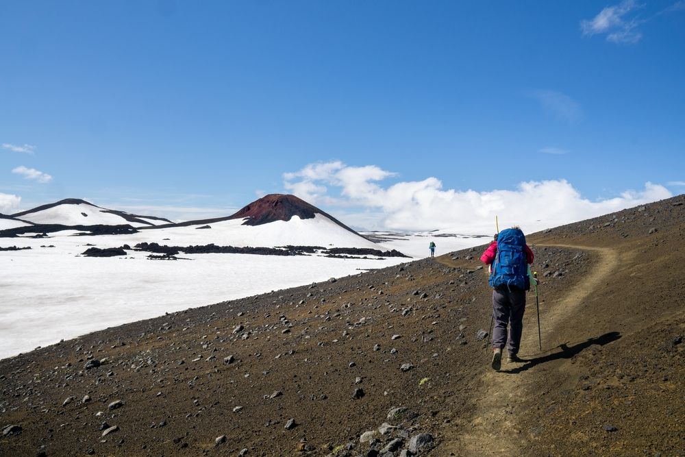 Hiker walking along a volcanic path surrounded by black sand and snowfields near Landmannalaugar in Iceland