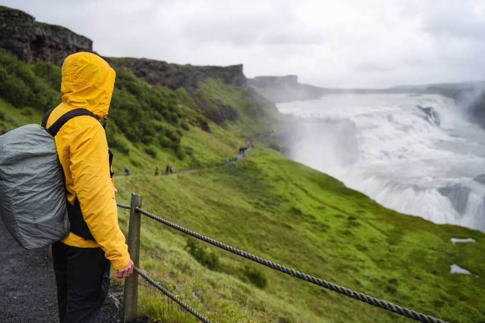 Visitor in outdoor outfit standing next to Gullfoss waterfall in Iceland during spring.