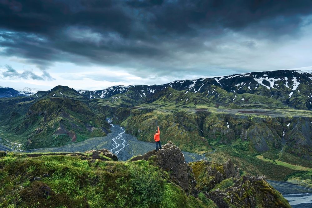 Hiker standing on a rocky peak overlooking dramatic green canyons and braided rivers in Þórsmörk, Iceland