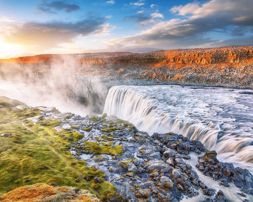 Sunrise lighting up the mist and basalt cliffs around Dettifoss waterfall in North Iceland.