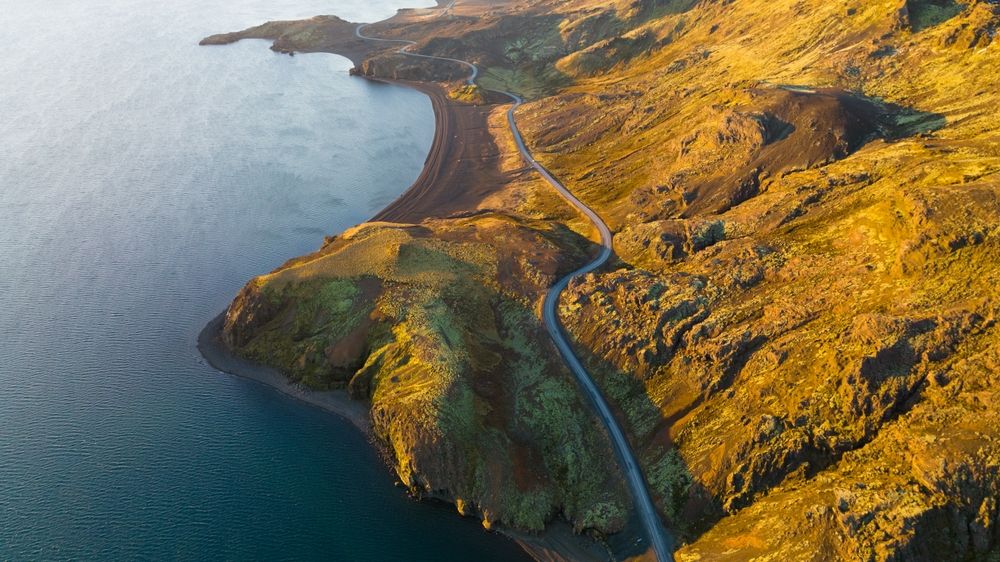 Aerial view of a winding road on Reykjanes Peninsula running along the dramatic coastline with volcanic terrain