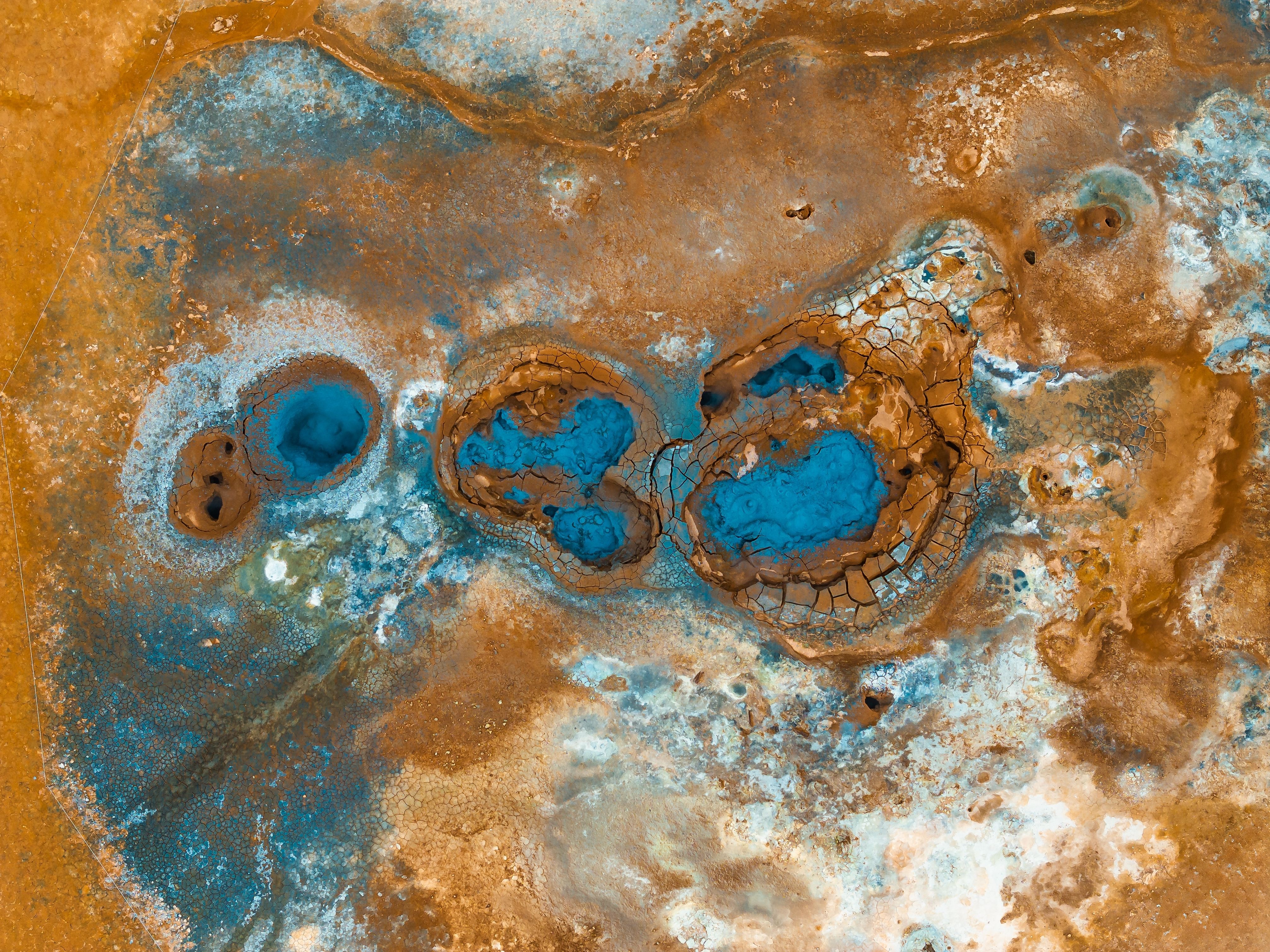 Drone view of bubbling blue mud pots and cracked mineral crust in the Hverir geothermal field in North Iceland
