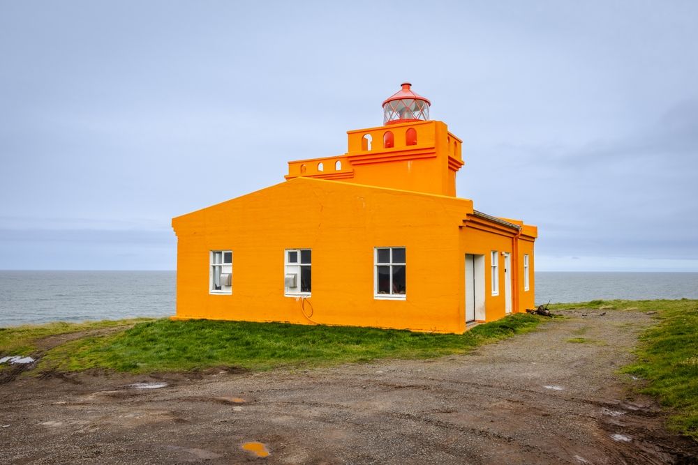 Bright orange lighthouse on a grassy cliff overlooking the sea in the Westfjords, Iceland.