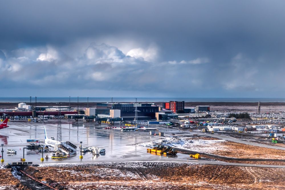 Aerial view of Keflavík International Airport with grounded airplanes and dramatic coastal skies.