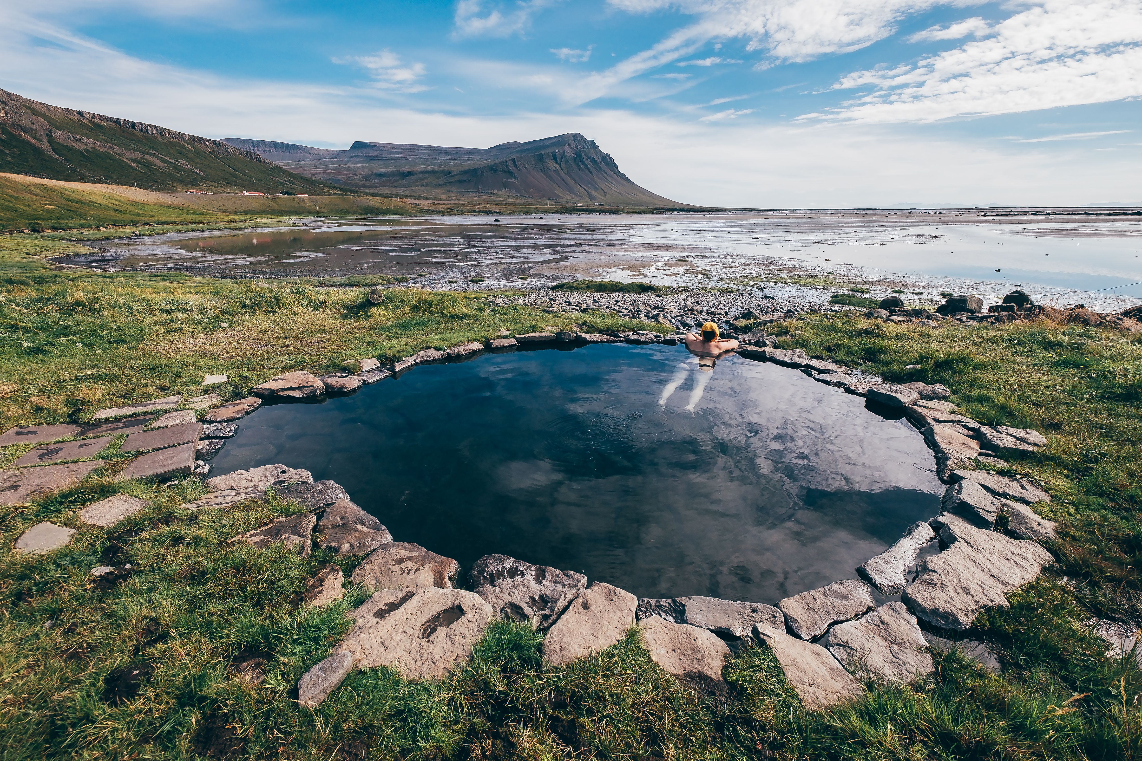 Traveler relaxes in Hellulaug hot pot, a natural geothermal pool overlooking a scenic fjord in Iceland’s Westfjords